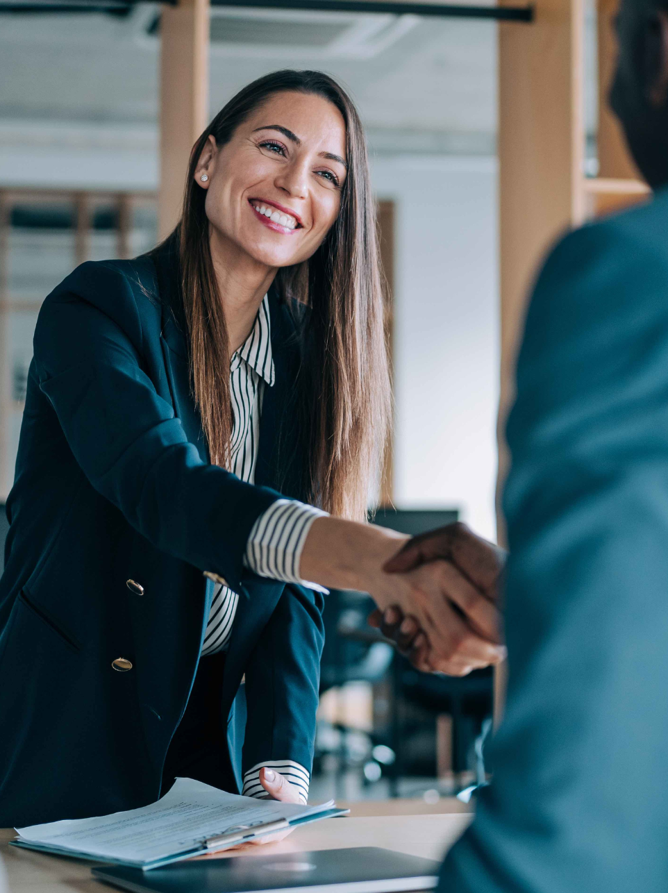 A businesswoman in a suit smiles as she shakes hands with someone in an office setting, exemplifying the success of strategic business and tax planning.
